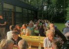 Menschen sitzen bei sommerlichem Wetter in einem Garten an gedeckten Tischen.